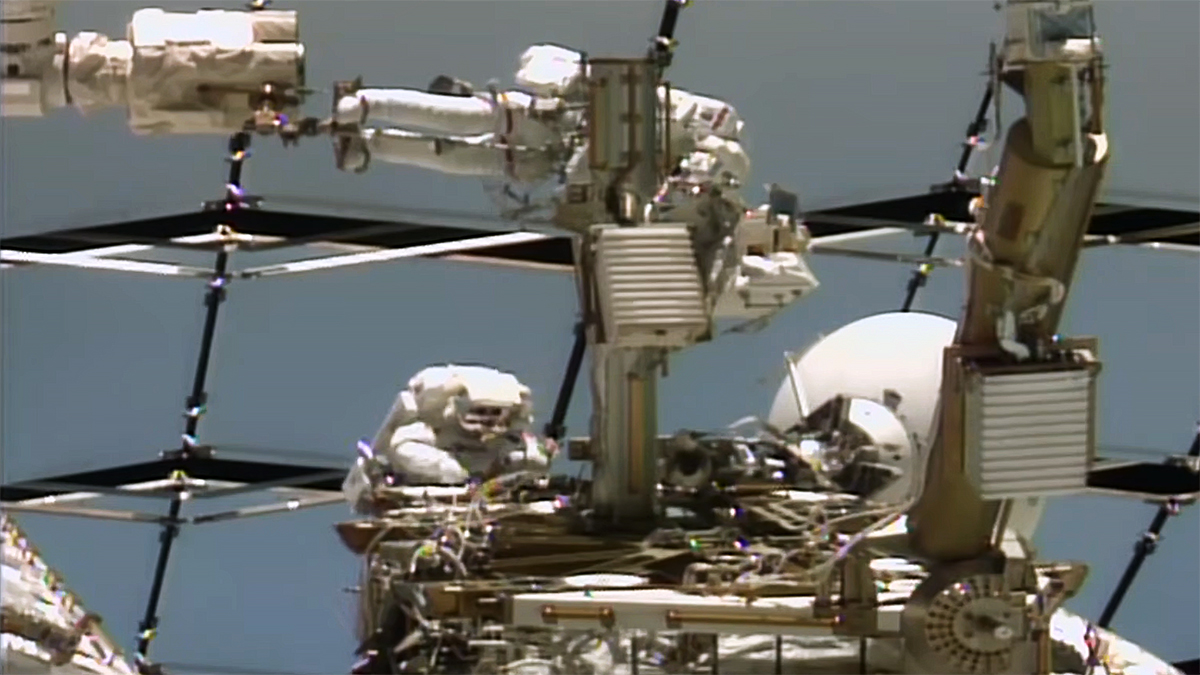 Anil Menon and Sophie Adenot work at the Z-1 truss during U.S. Spacewalk 97 on August 18, 2026 — the failed Space-to-Ground antenna they removed and tied down on the structure. (NASA)
